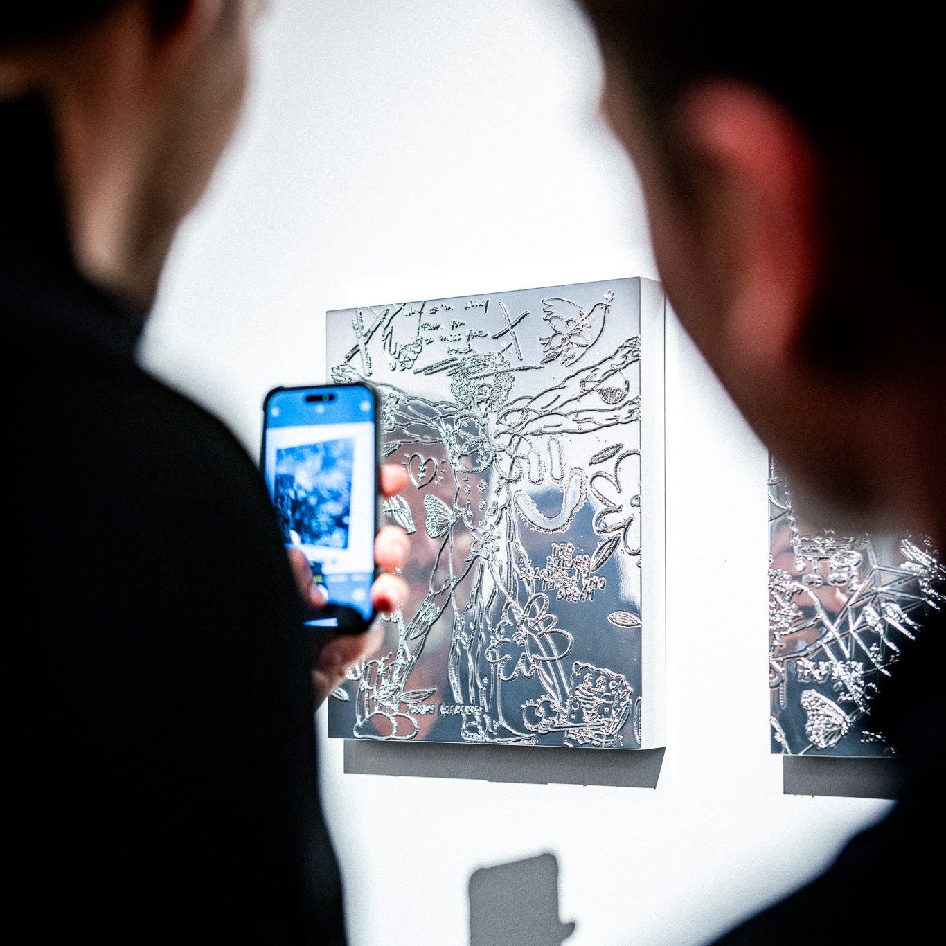 Two people taking a photo of a Chrome Painting Collectible by Joseph Klibansky with a phone.