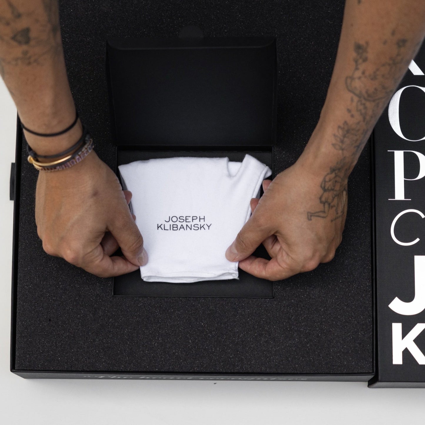 Person opening a black box containing a white towel with 'Joseph Klibansky' branding, against a white background.