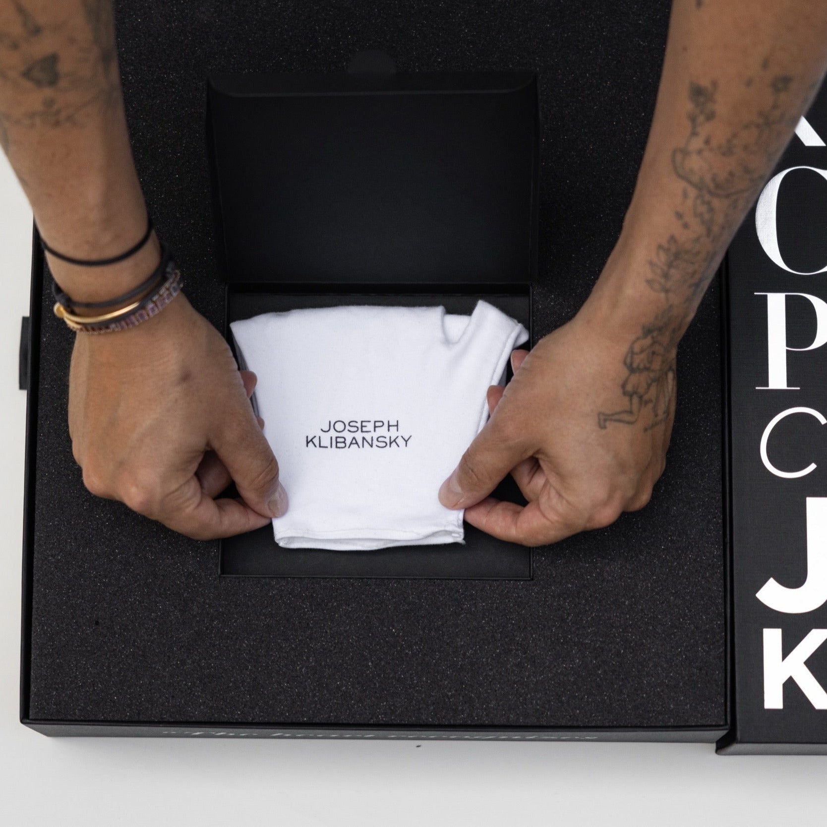 Person opening a black box containing a white towel with 'Joseph Klibansky' branding, against a white background.
