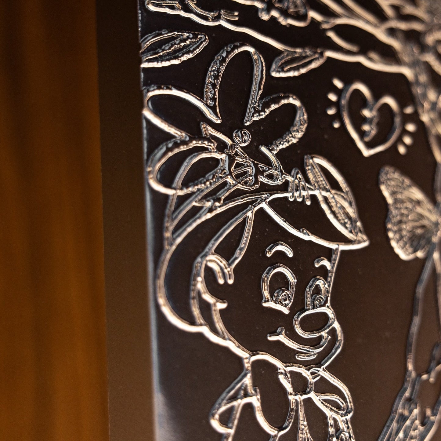 Decorative metal panel with engraved floral and butterfly design on a wooden background