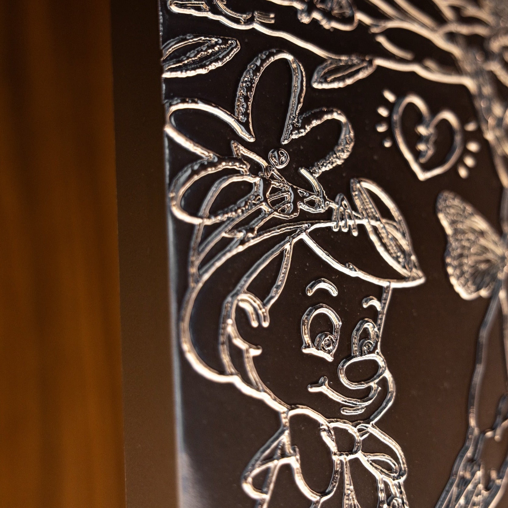Decorative metal panel with engraved floral and butterfly design on a wooden background