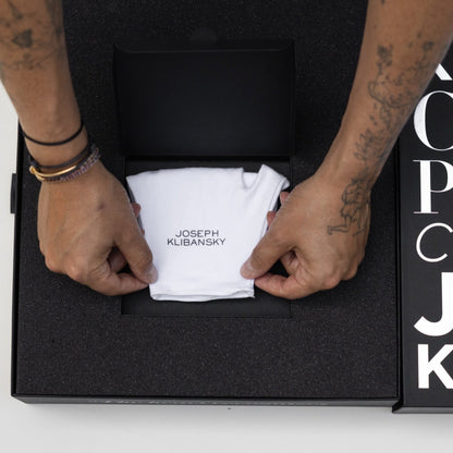 Person opening a black box containing a white towel with 'Joseph Klibansky' branding, against a white background.