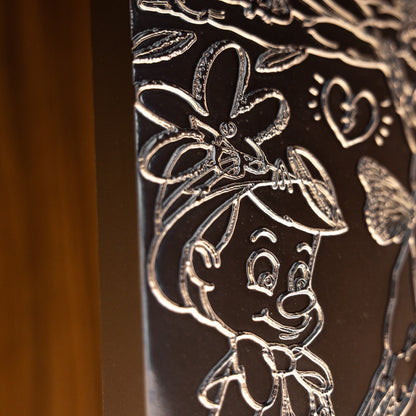 Decorative metal panel with engraved floral and butterfly design on a wooden background